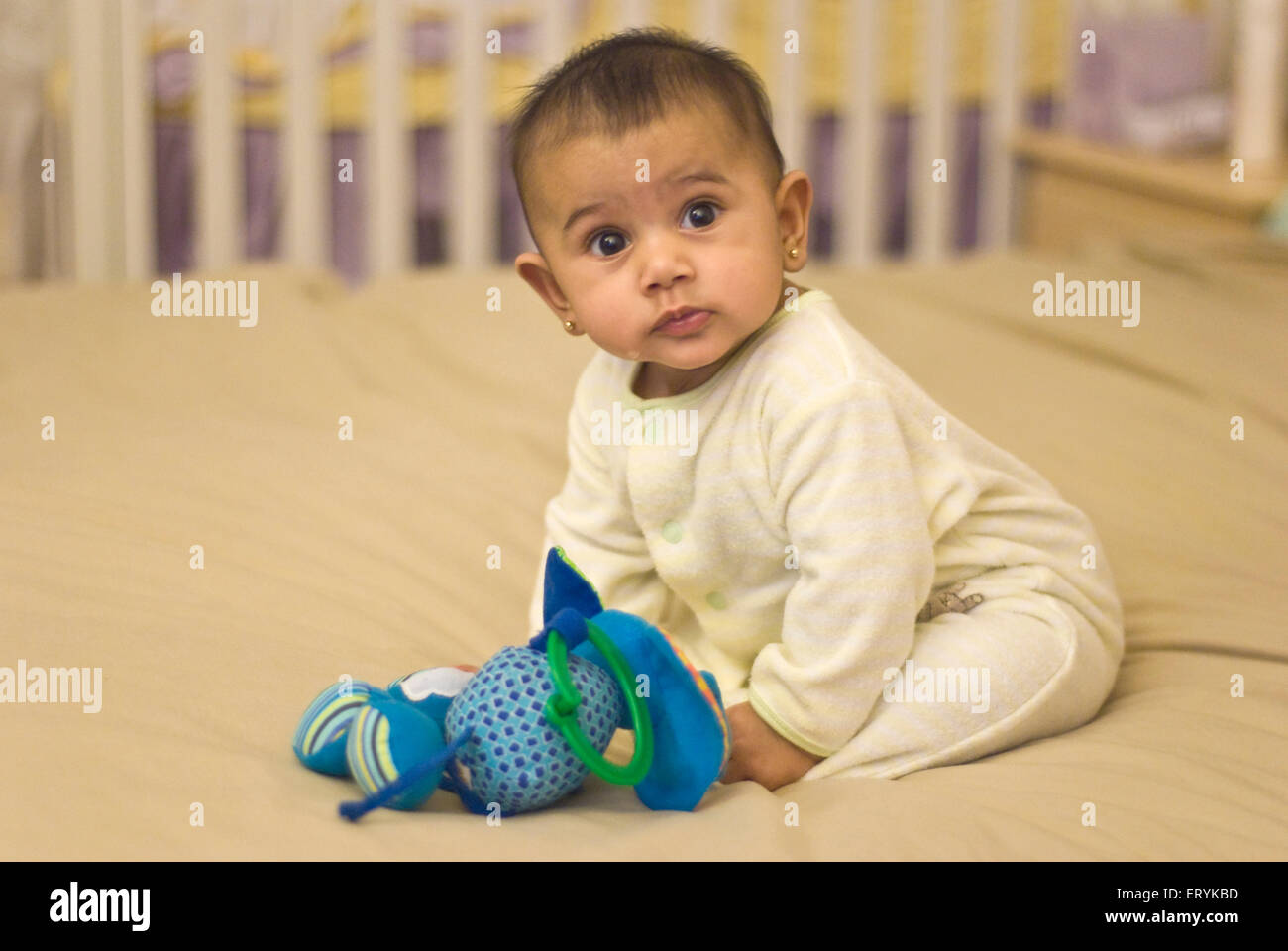 Six months old baby girl sitting on bed with cuddly toy , MR#447G Stock Photo