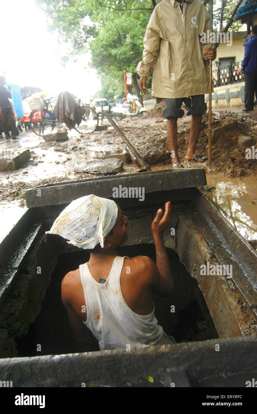Man cleaning drainage pipe in rain , Bombay , Mumbai , Maharashtra