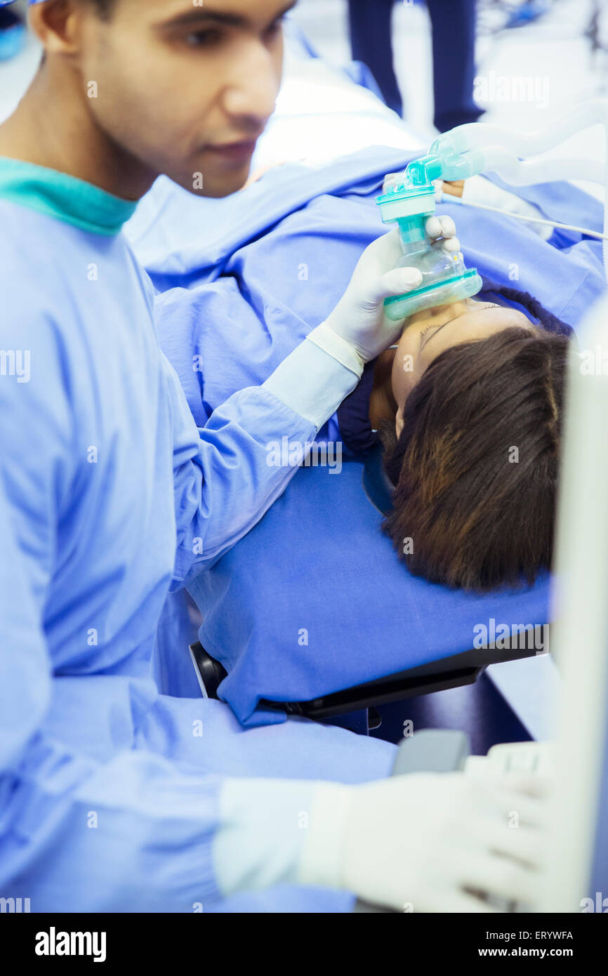 Anesthesiologist holding oxygen mask over patient’s face in operating room Stock Photo