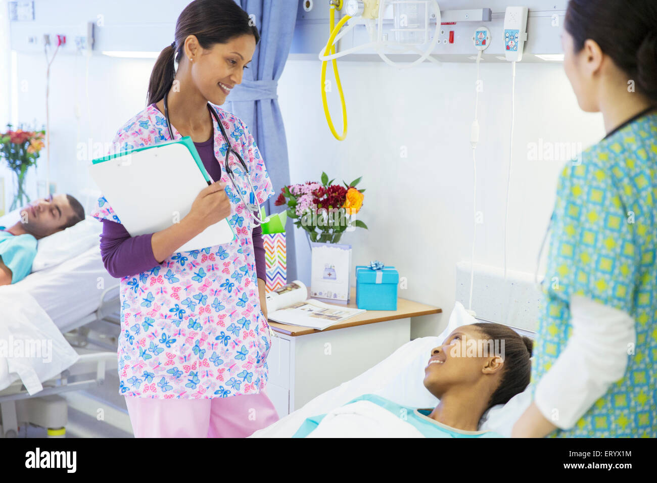 Smiling nurses talking with patient in hospital room Stock Photo