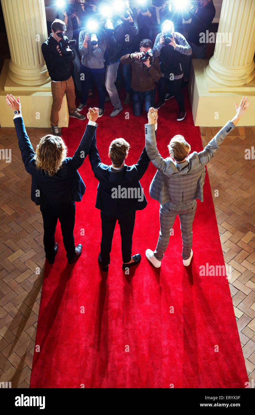 Celebrities holding hands with arms raised for paparazzi photographers at red carpet event Stock Photo