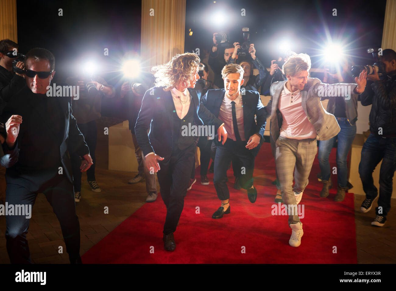 Enthusiastic celebrities arriving and running from paparazzi at red carpet event Stock Photo