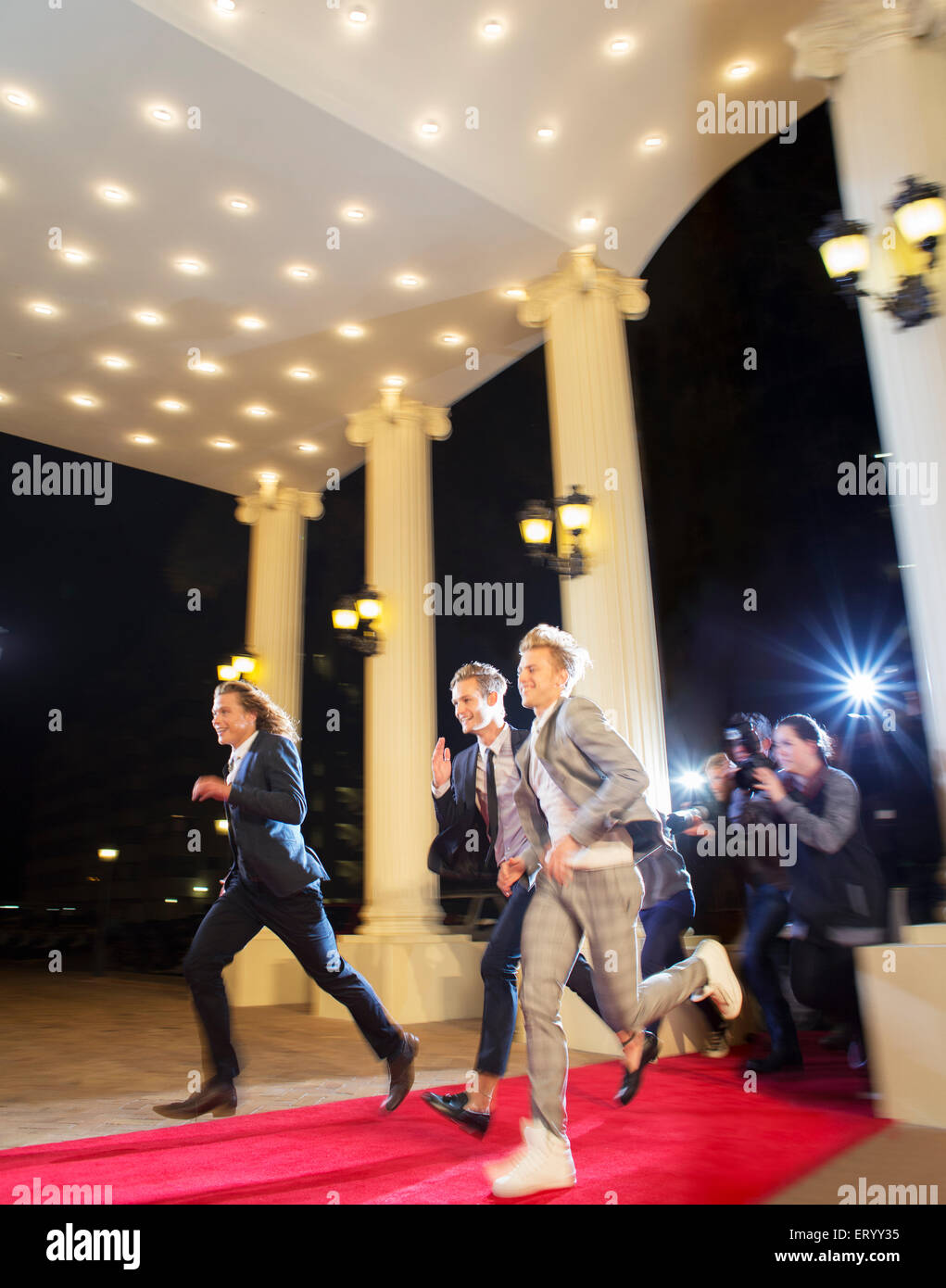 Enthusiastic celebrities arriving and running from paparazzi photographers at red carpet event Stock Photo