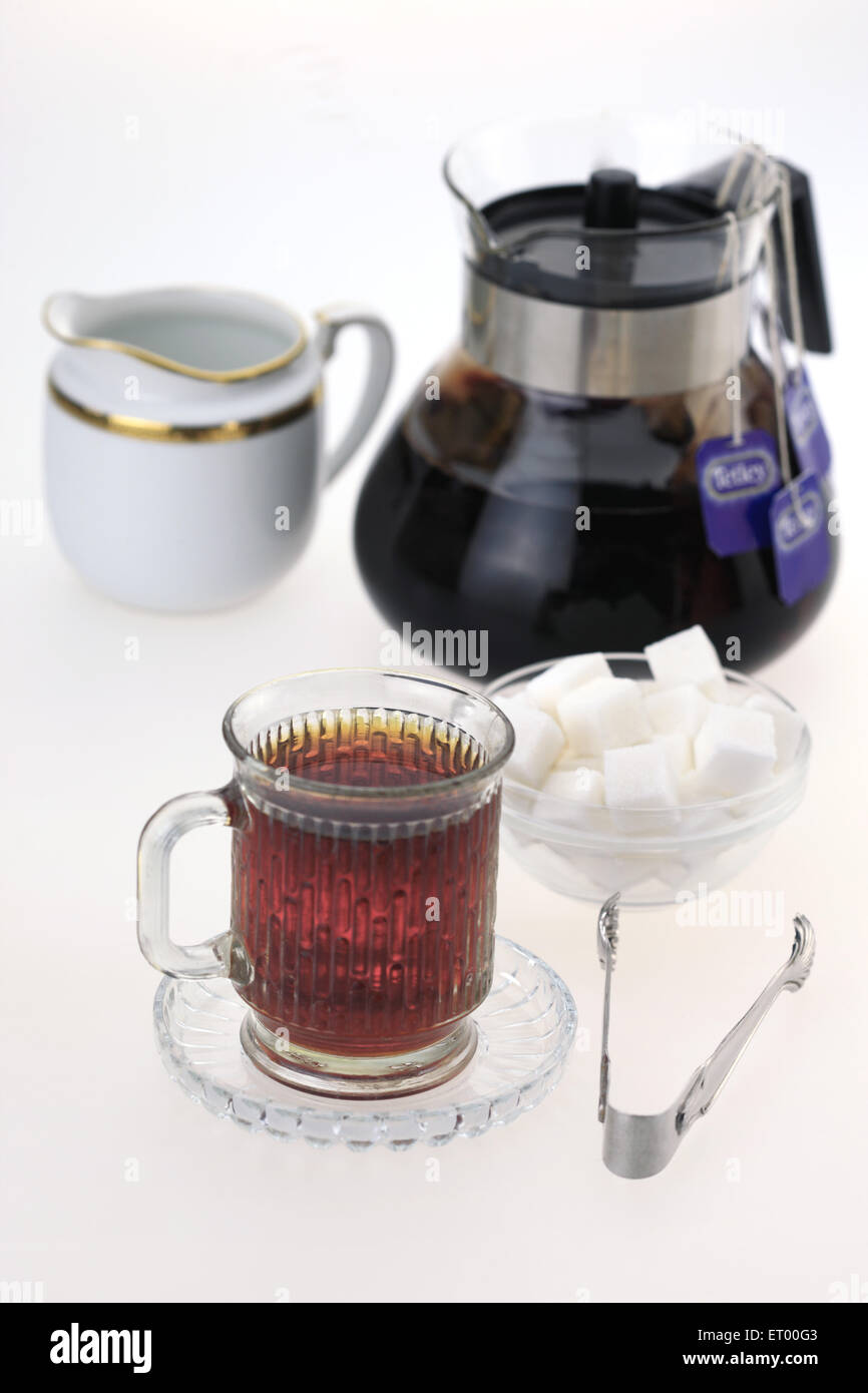 Mug of hot black tea with sugar cubes ; milk pot ; tongs and kettle