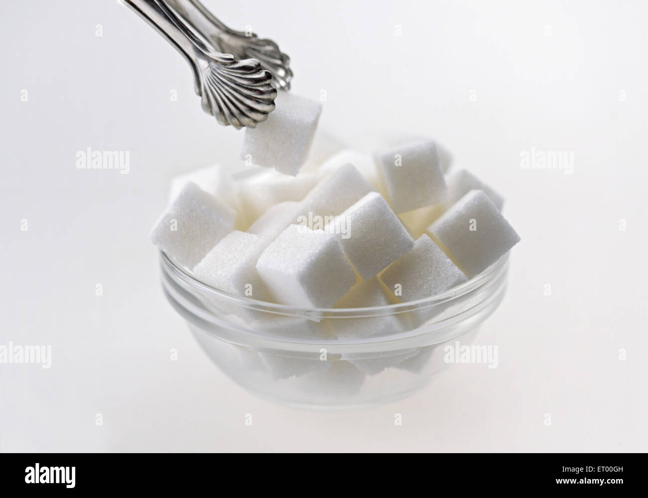 Sugar cubes in a glass bowl with tongs Stock Photo