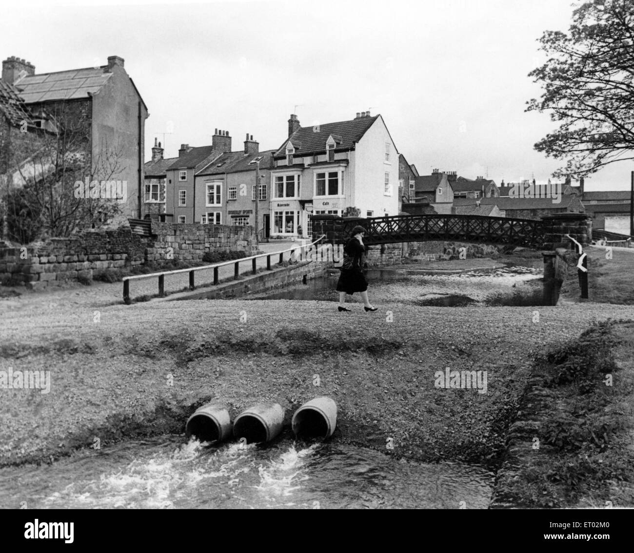 They're 'walking on water' in novel style down Stokesley way these days, The metal road bridge off the HIgh Street is showing signs of corrosion in its metal beams and North Yorkshire engineers are to replace them with pre-cast concrete ones. As work goes on for several weeks this dam style 'bridge' will take foot and motor traffic - but three 12 inch diameter pipes make sure the Leven doesn't overflow in the meantime. 1st May 1981. Stock Photo