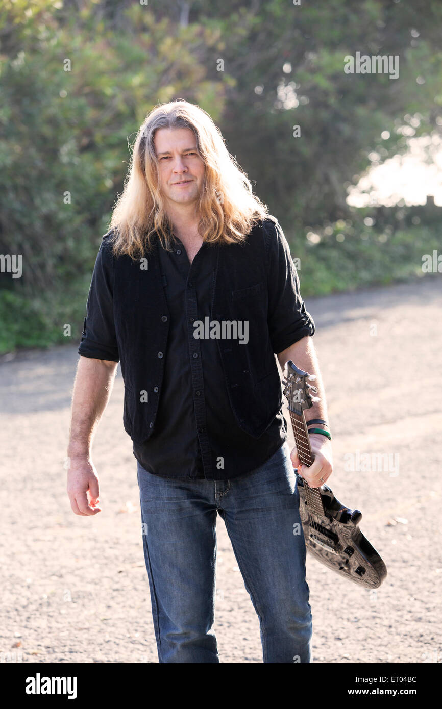 Long Haired Man With A Guitar Walking On A Street Stock Photo