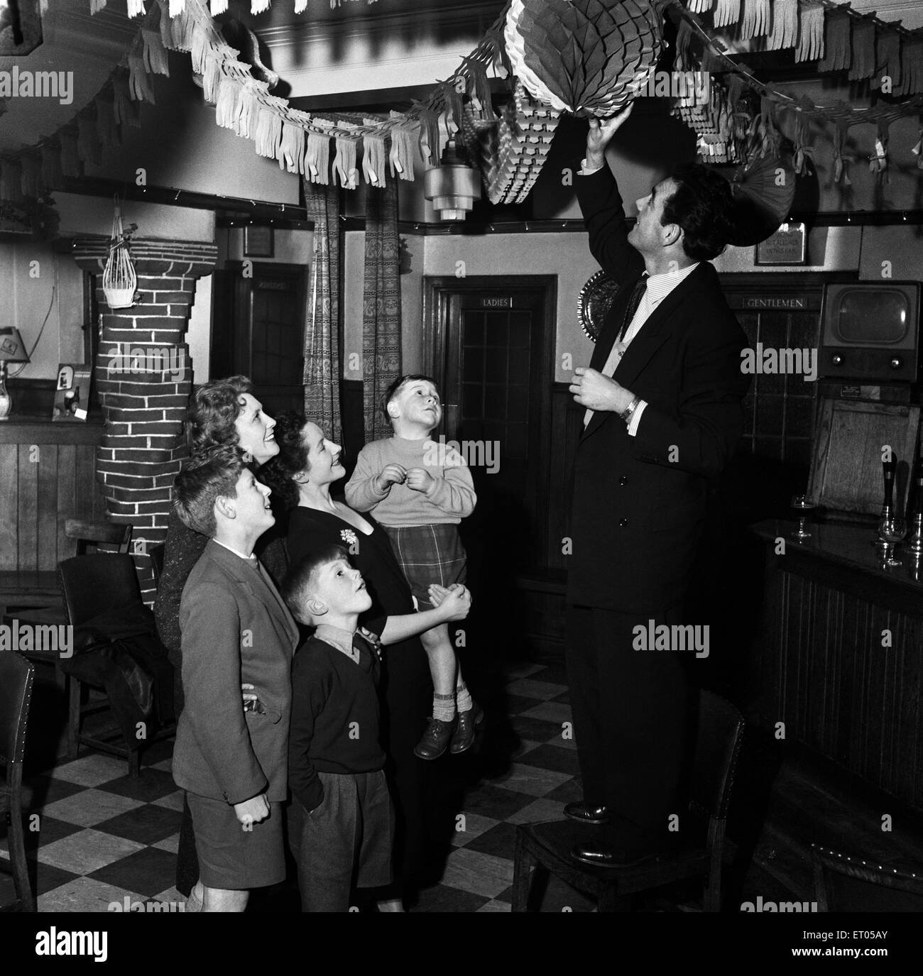 Charlton Athletic footballer Johnny Summers who just scored five goals in one game in the spectacular fightback from 6-1 down to 7-6 winners against Huddersfield.  Here he is pictured putting up the Christmas decorations at the Arrows pub off the Old Kent Road watched by his wife Betty and their son John.  22nd December 1957. Stock Photo
