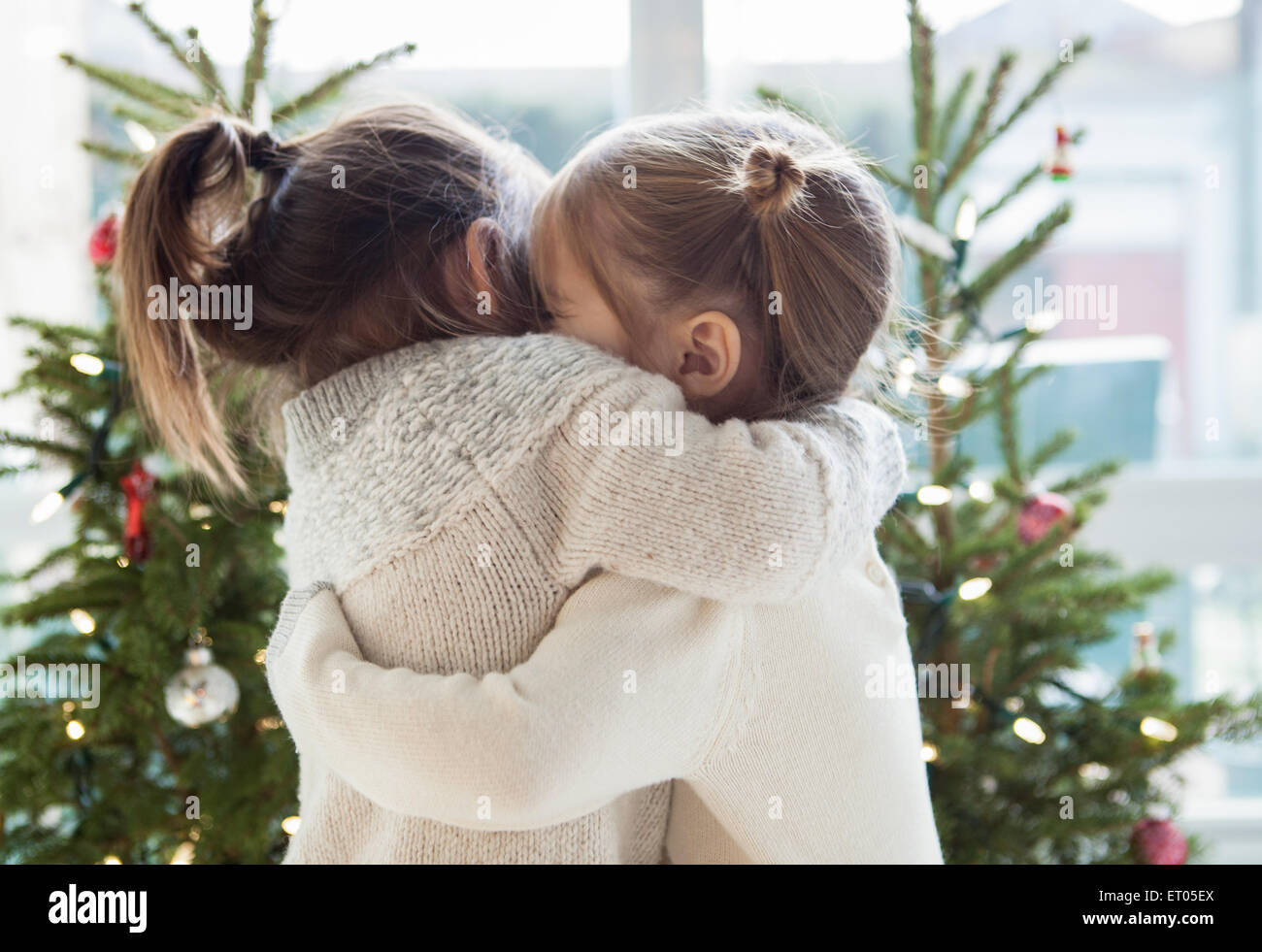 Girls hugging in front of Christmas trees Stock Photo