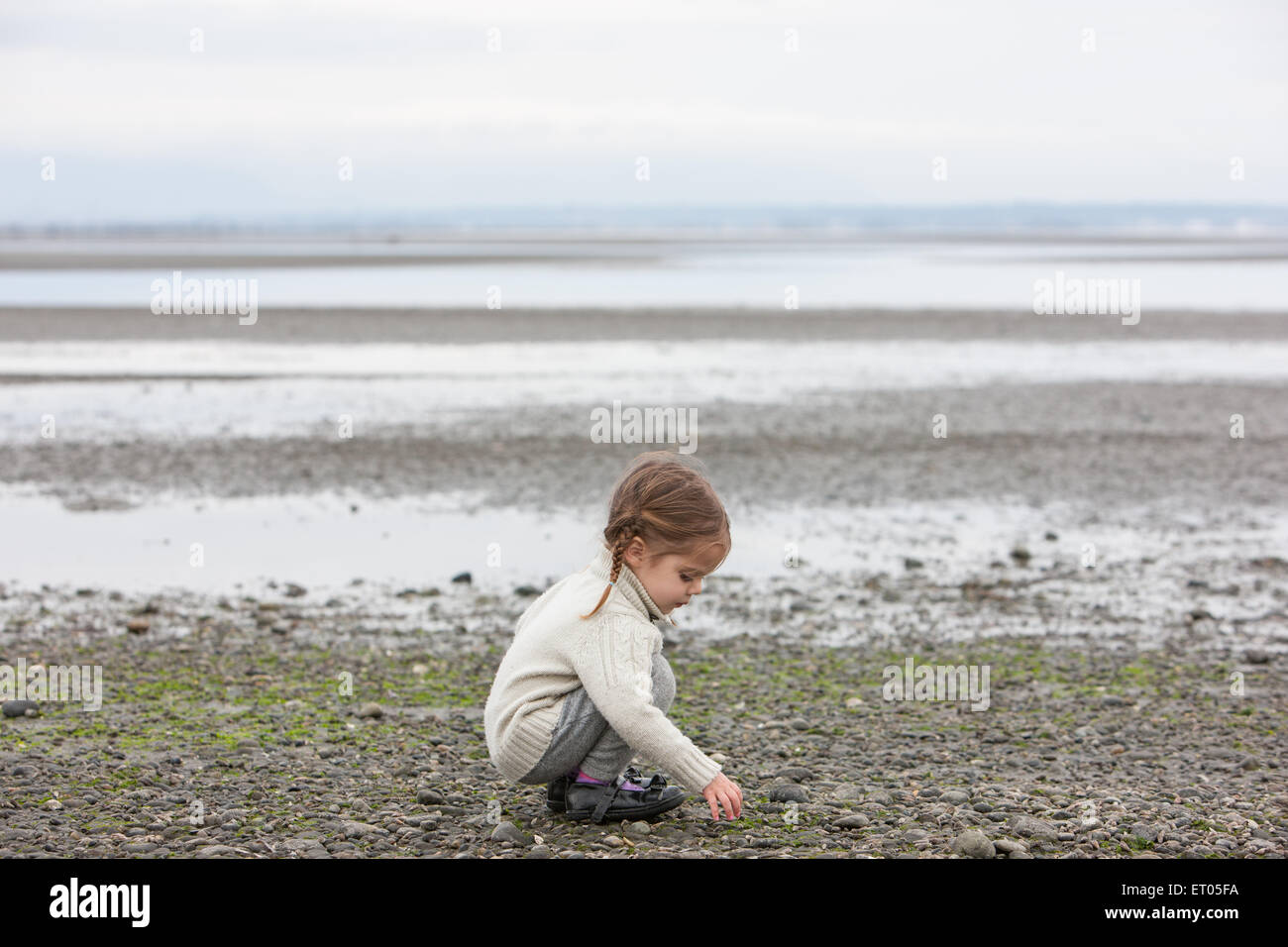 Girl picking up pebbles on beach Stock Photo