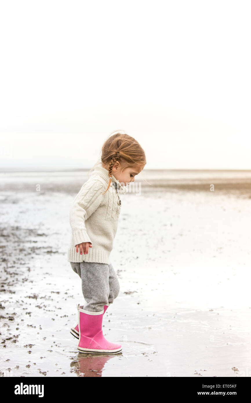 Girl in pink rain boots playing in water on beach Stock Photo
