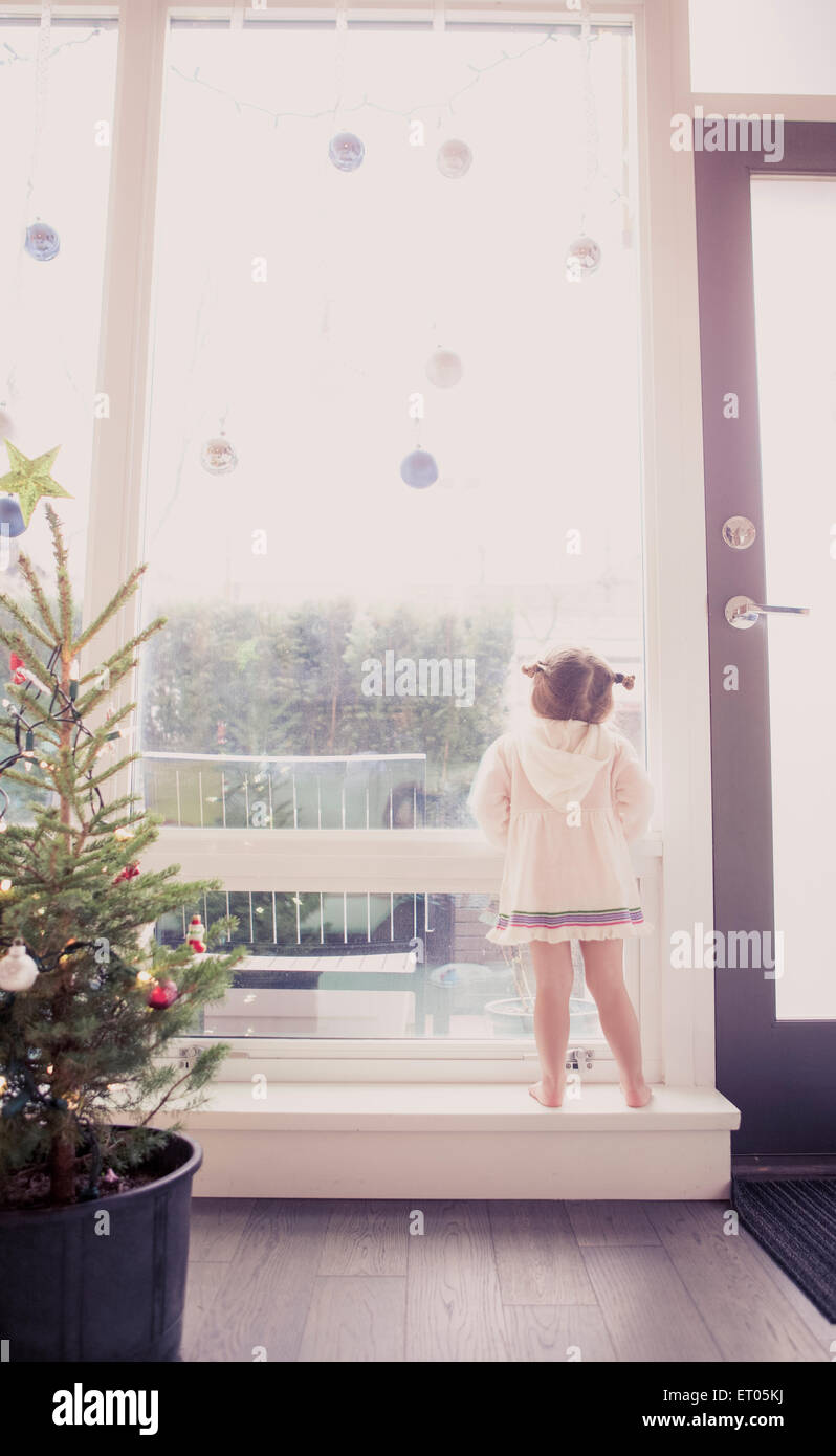 Curious girl on window ledge below Christmas ornaments Stock Photo