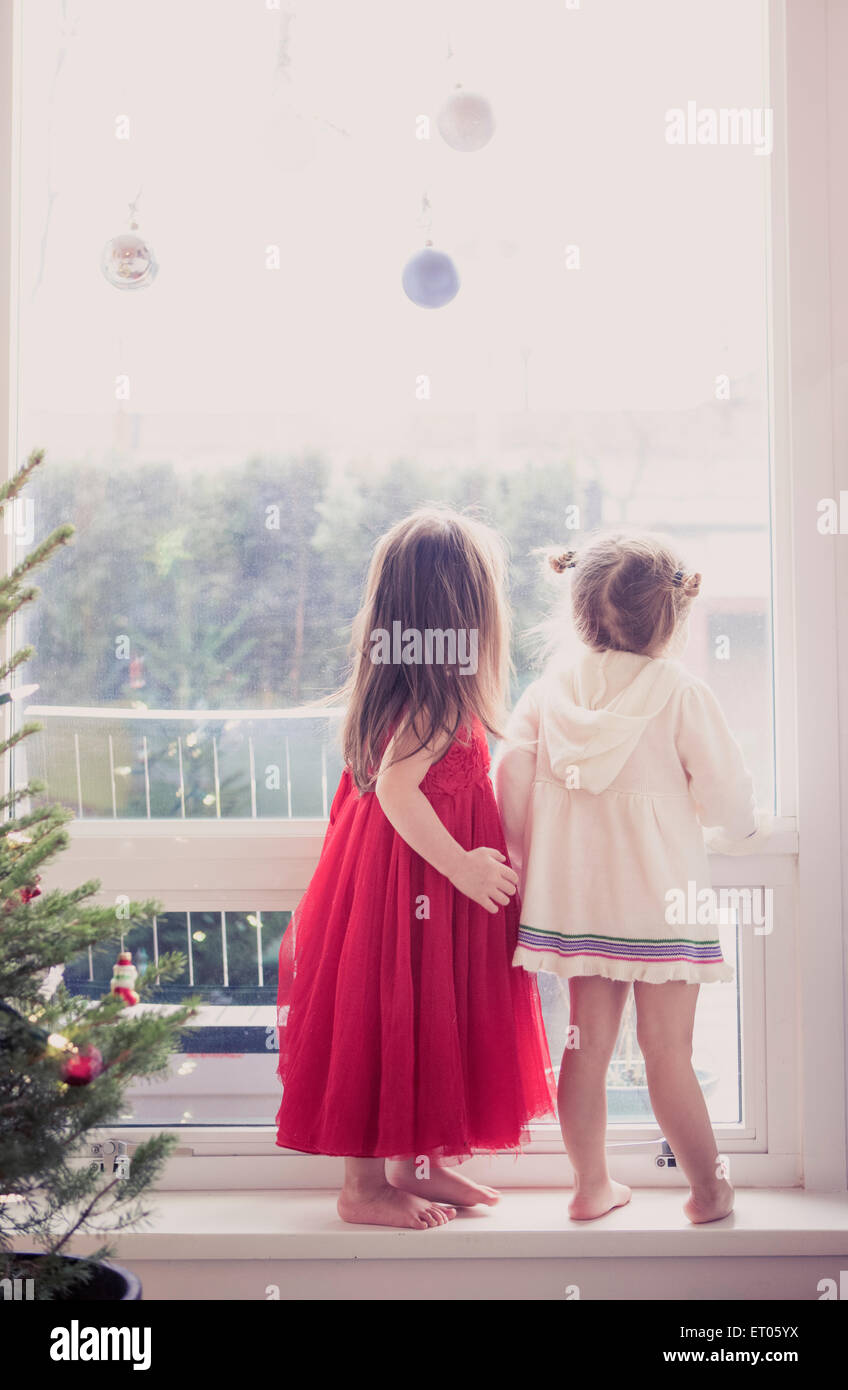 Girls on window ledge below Christmas ornaments Stock Photo