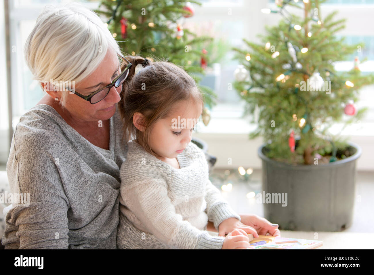 Grandmother watching granddaughter drawing in front of Christmas trees Stock Photo