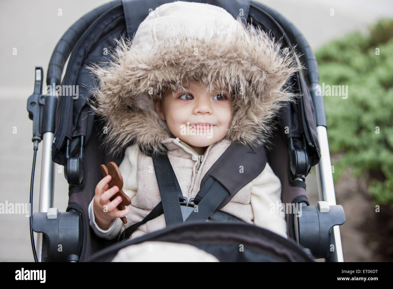 Smiling girl in fur hood riding in stroller Stock Photo