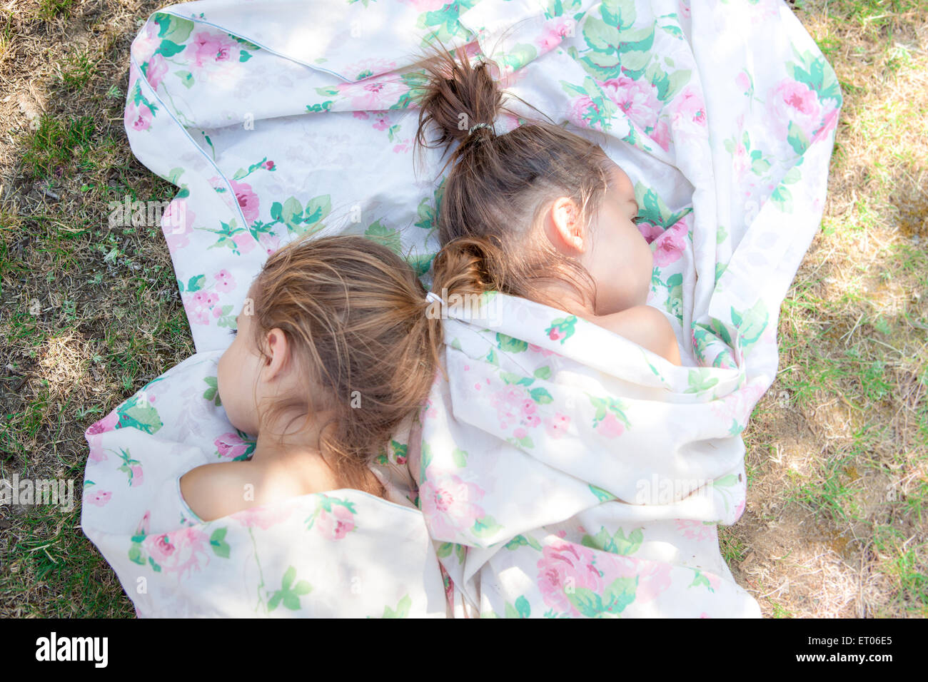 Twin girls napping in floral sheet on grass Stock Photo