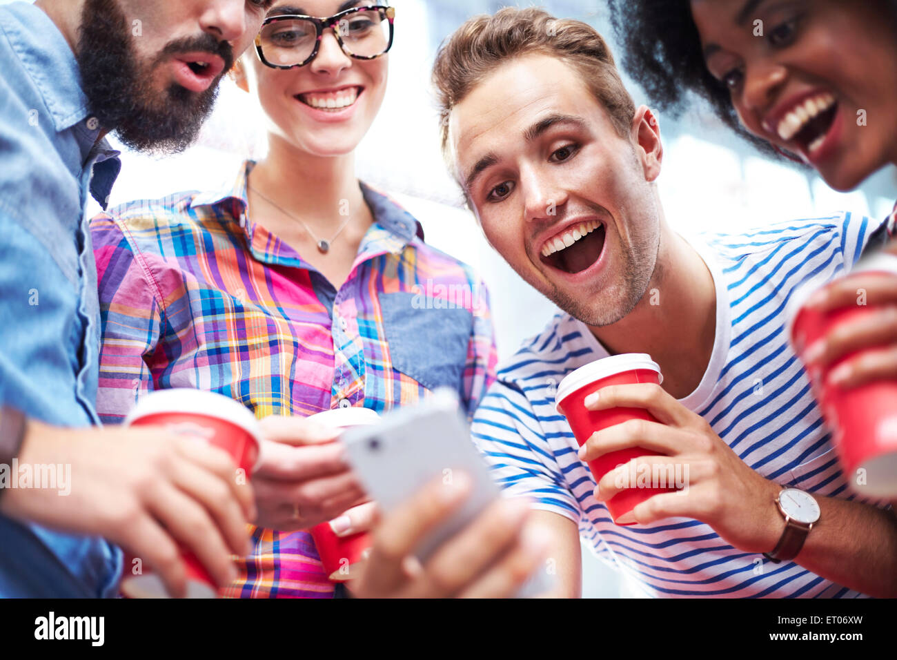 Friends laughing and drinking coffee around cell phone Stock Photo
