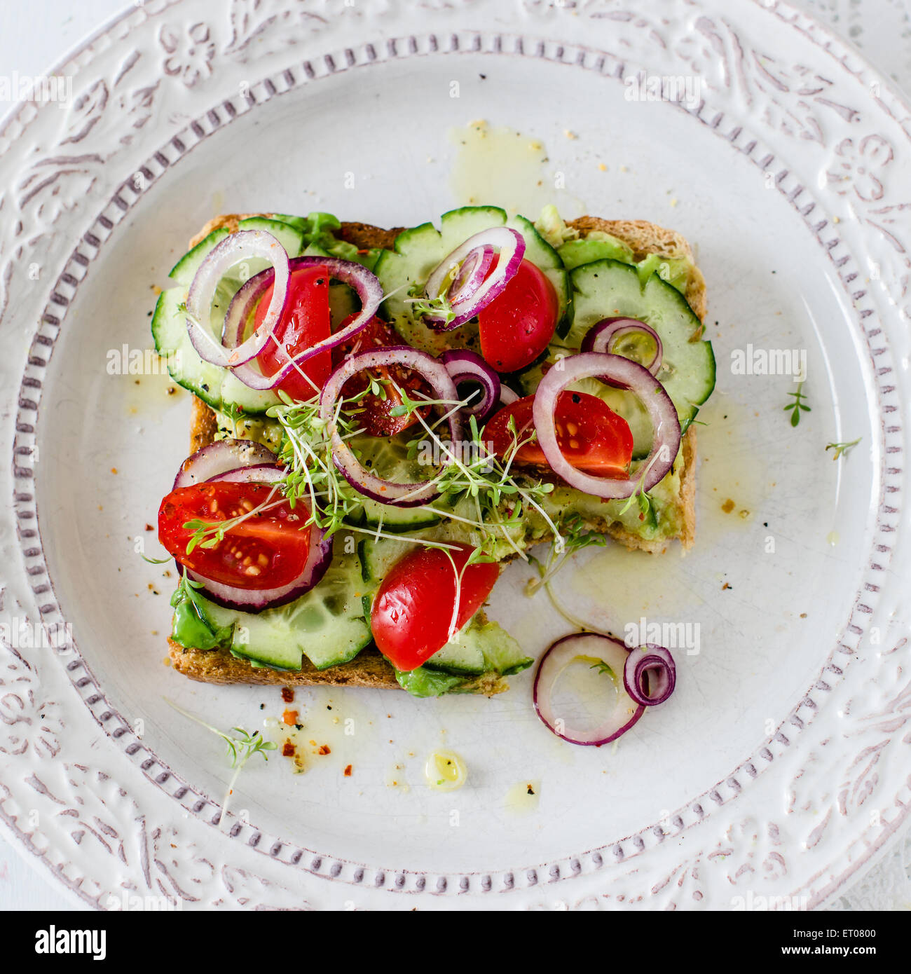 vegan sandwich with avocado and vegetables, missing one bite. Stock Photo