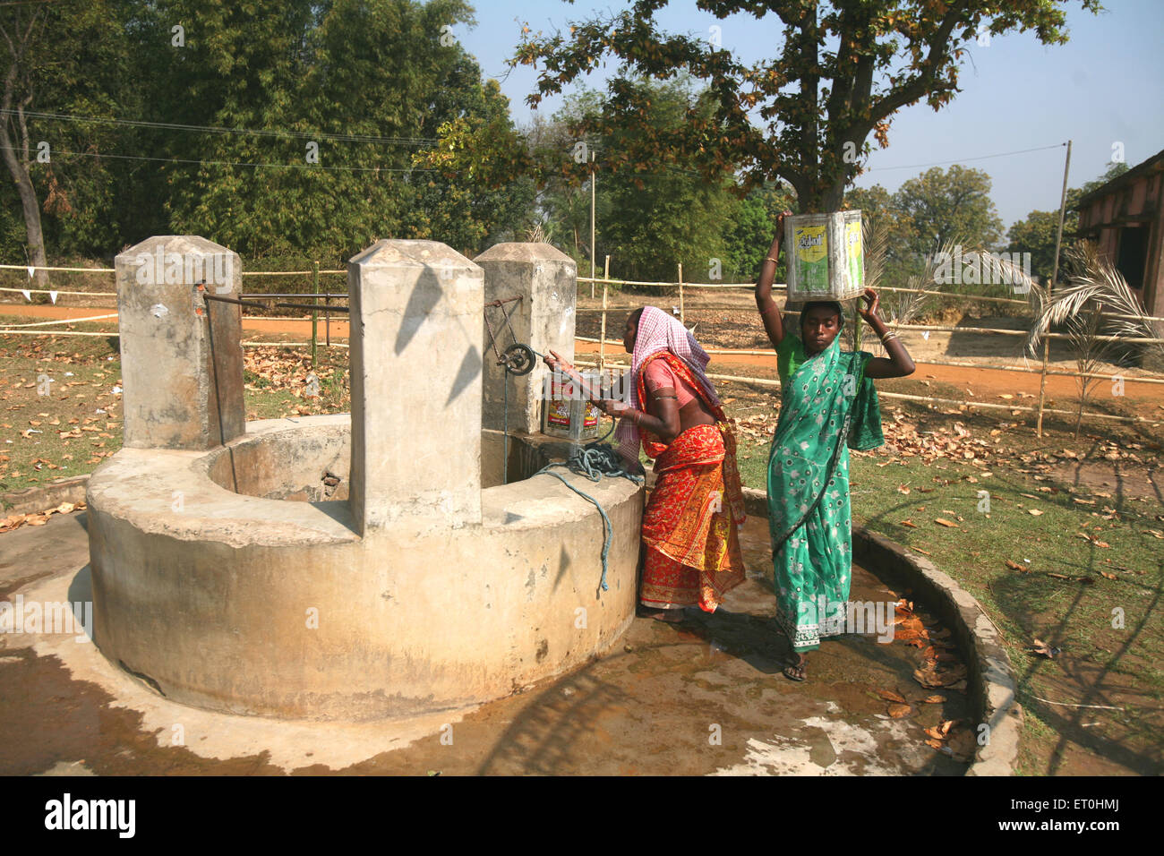 Lady drawing water from well while one carrying water on her head in Jharkhand ; India Stock Photo