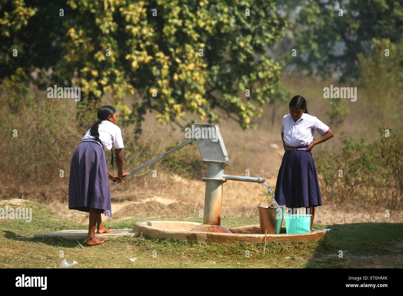 School children girls in school uniform drawing water from hand pump in Jharkhand ; India Stock Photo