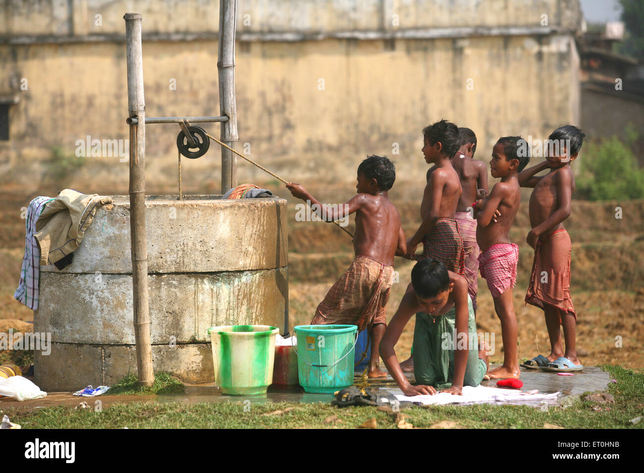 Children drawing water from well to take bath boy washing clothes at well i...