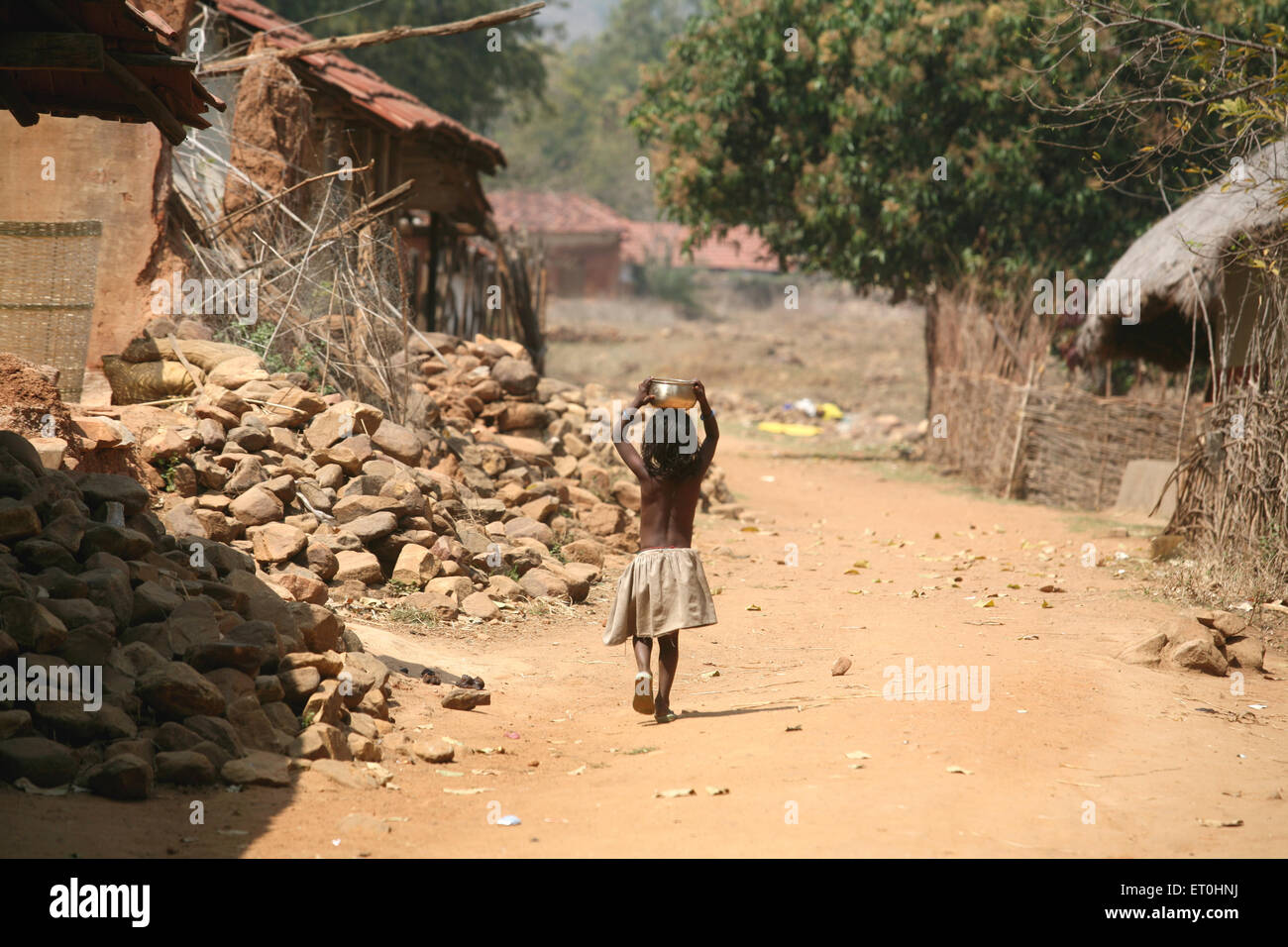 Young girl carrying utensil over her head walking through village houses in Jharkhand ; India Stock Photo