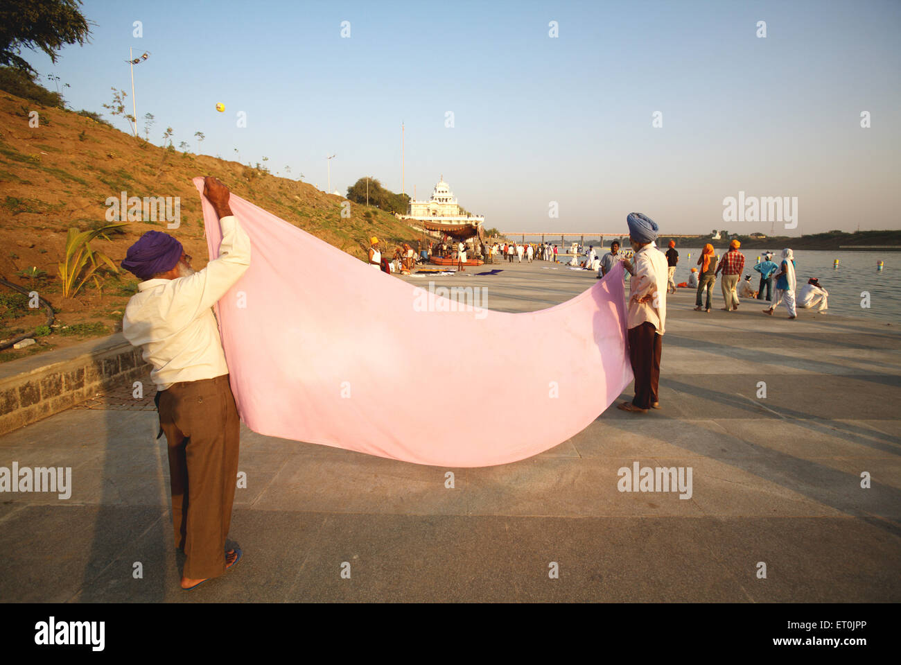 Sikh devotees drying traditional 6 meter long headgear or on 15 km long Ghat of river Godavari after holy bath ; Nanded Stock Photo
