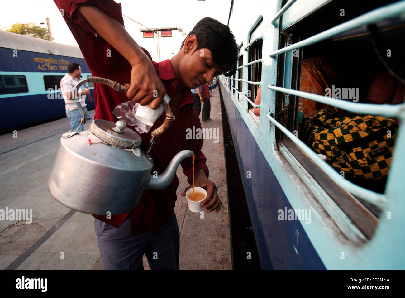 Indian railway tea vendor pouring tea from aluminium kettle into Stock