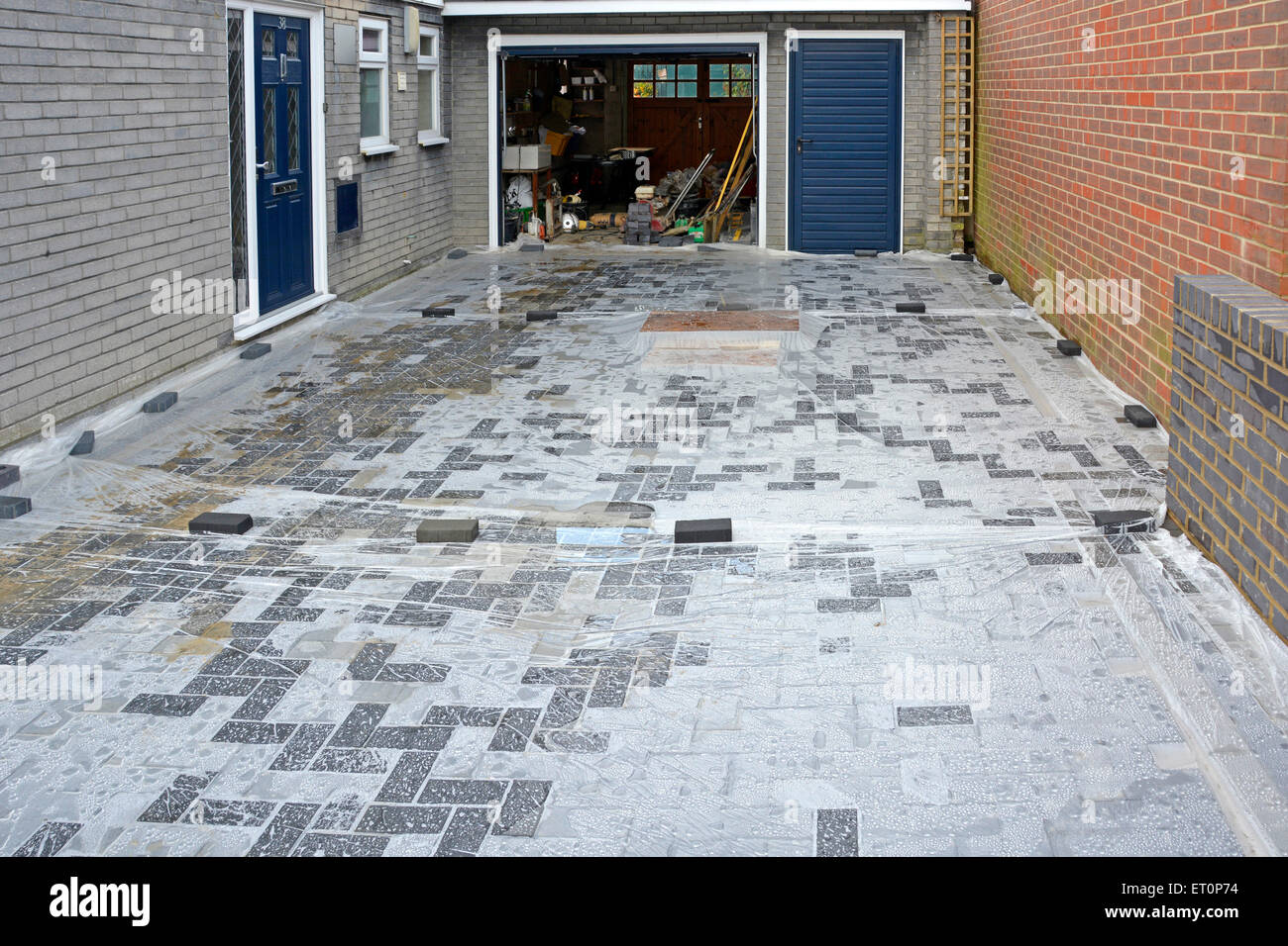 Home improvements new car driveway plastic sheeting laid onto block paving to stop storm weather reaching sand sub base before completion England uk Stock Photo