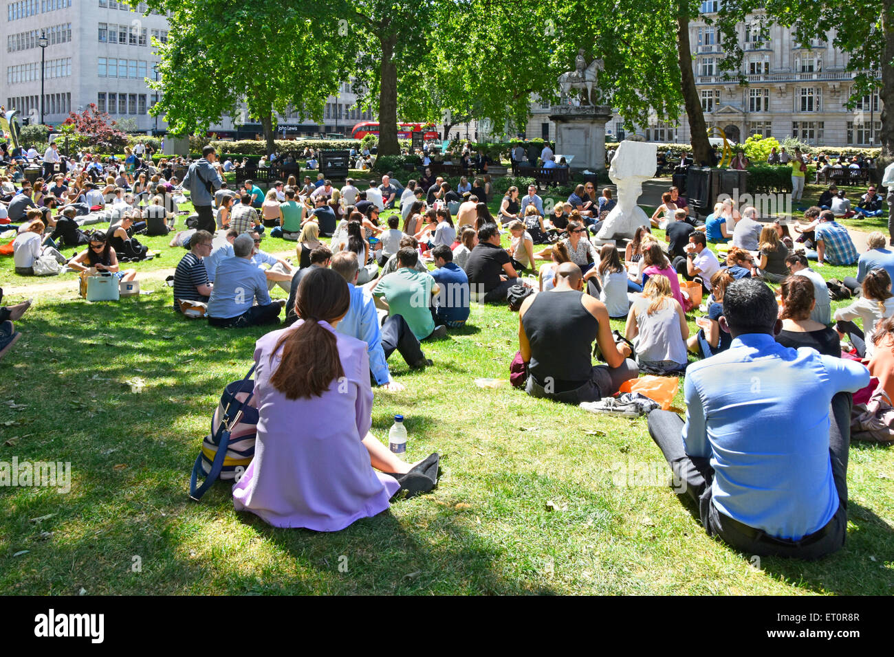 London people in Cavendish Square gardens mainly office and shop workers sitting on grass at lunch time break on a warm summer day London England UK Stock Photo