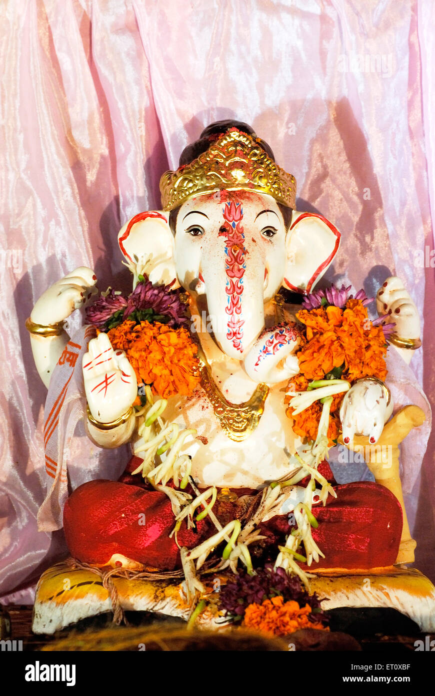 Small idol of Lord Ganesh wearing garland of flowers elephant headed god ; Ganapati festival at Pune ; Maharashtra ; India Stock Photo