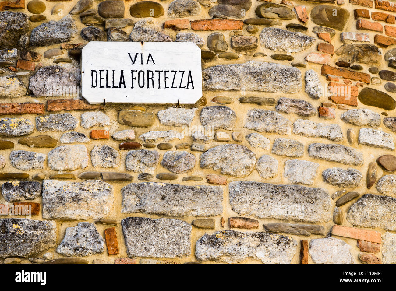 Italian sentence, Via della Fortezza on sign nailed on wall made by smooth stones: meaning is Fortitude road or Fortress road Stock Photo