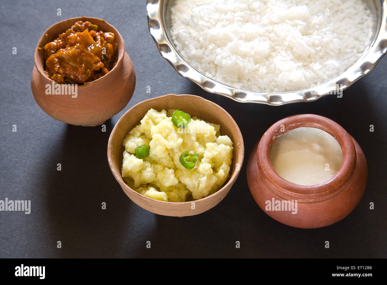 Indian lunch pakhala rice in steel bowl and pickle mash potato with chillies yoghurt in earthen pot black background Stock Photo
