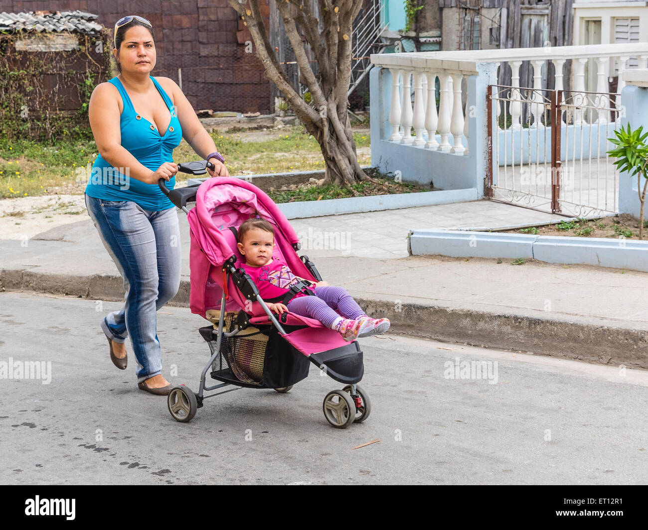 A thirty something Cuban mother walks, pushing her young son in his stroller in Santiago de Cuba. Stock Photo