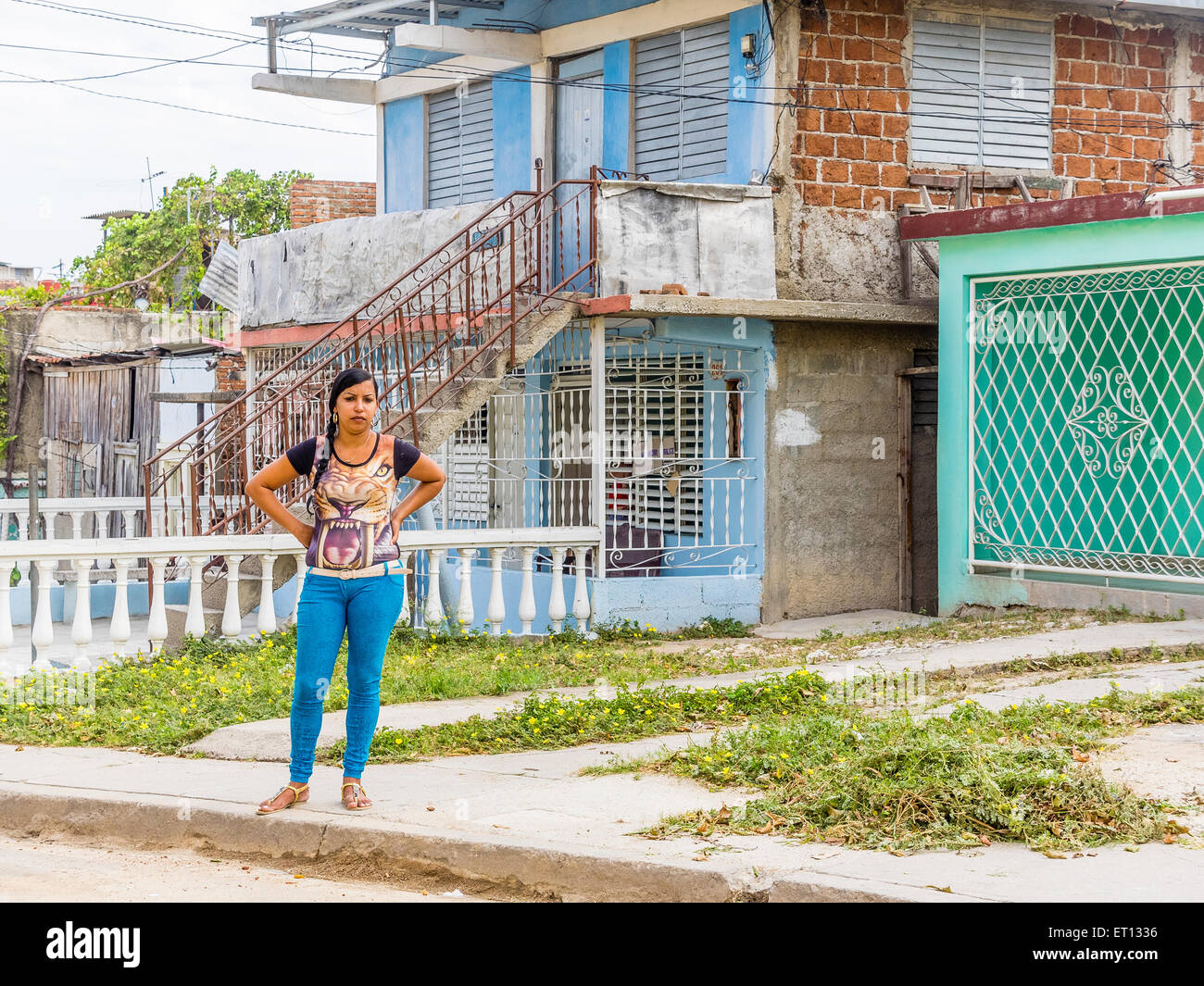 A twenty something Cuban woman stands with her hands on her hips, dressed in a tiger face blouse and turquoise pants. Stock Photo