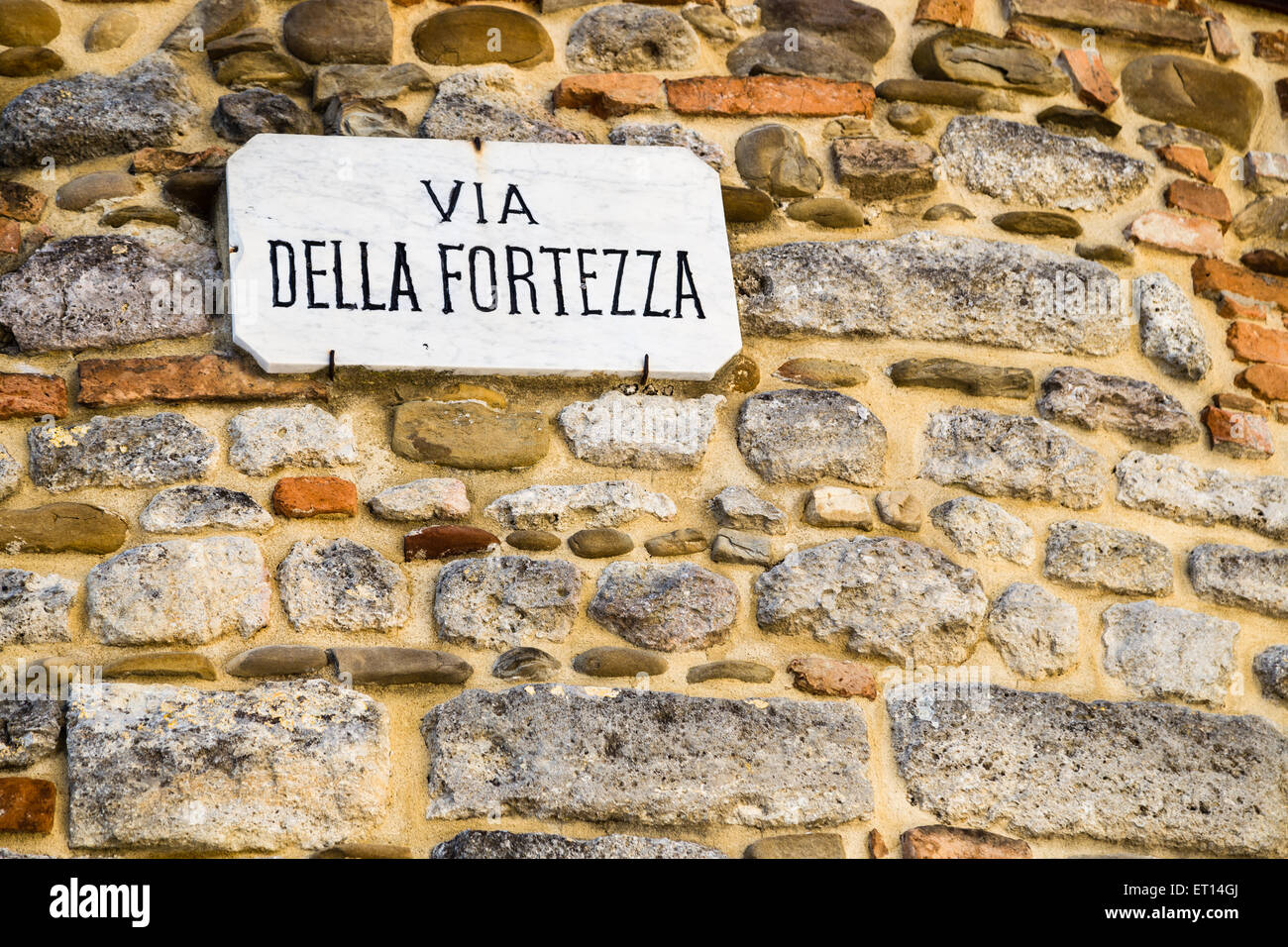 Italian sentence, Via della Fortezza on sign nailed on wall made by smooth stones: meaning is Fortitude road or Fortress road Stock Photo