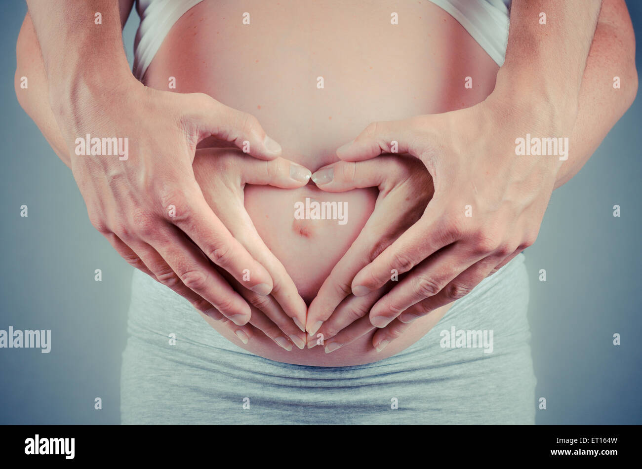 parents hands making a heart on the mothers belly Stock Photo