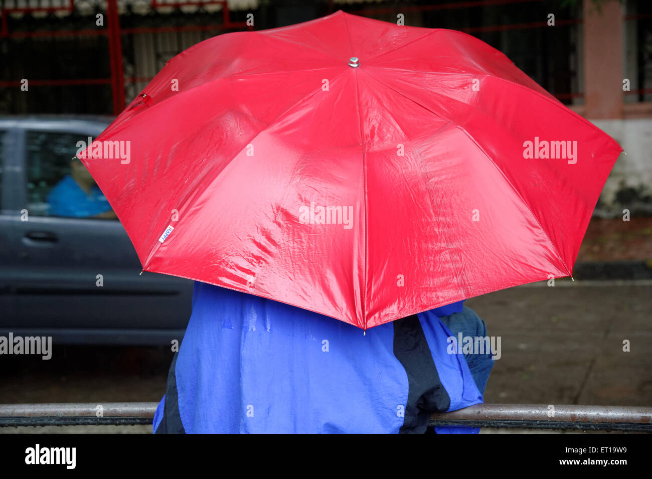 Man in blue plastic raincoat with red umbrella MR#364 Stock Photo