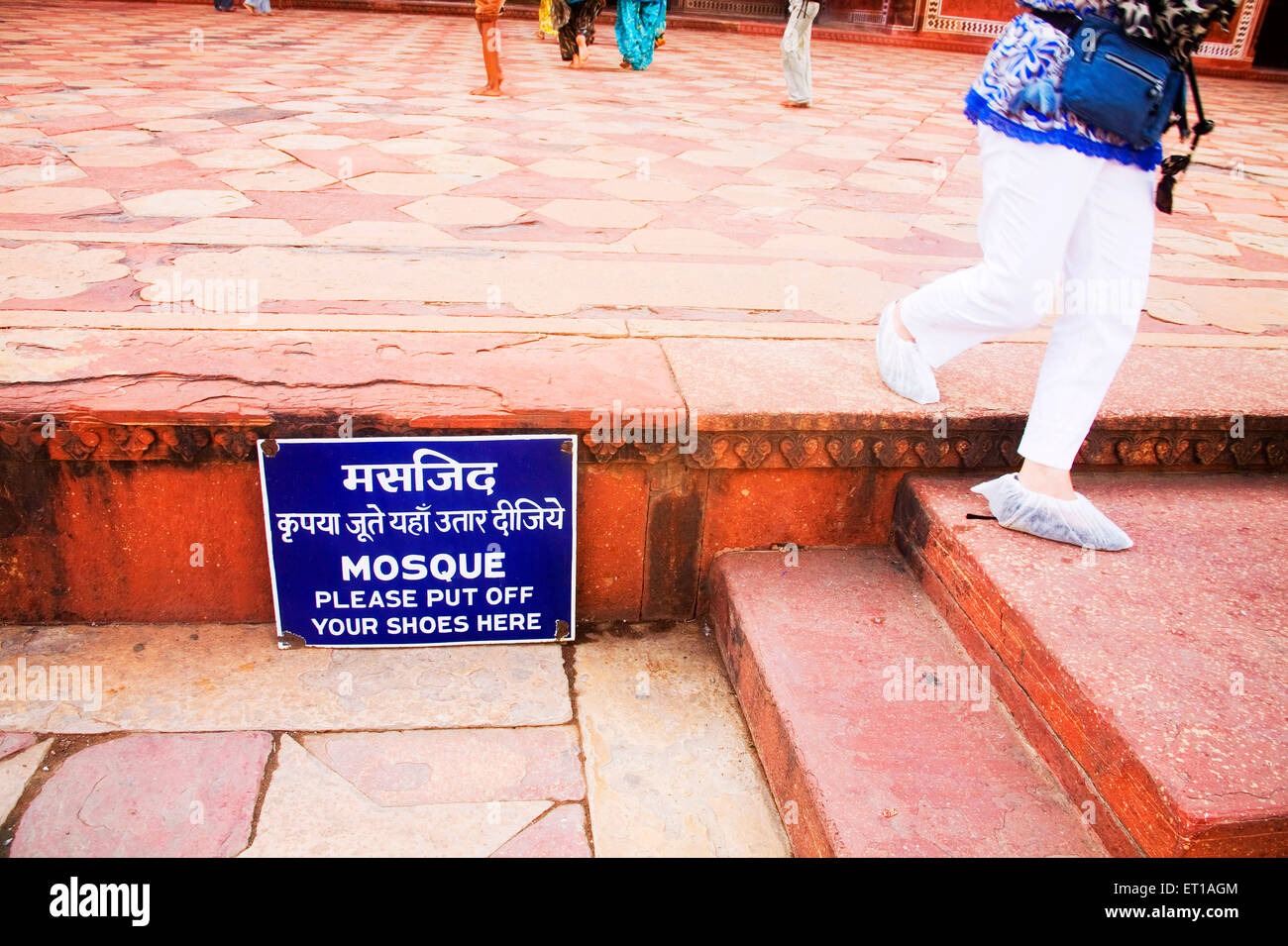Tourist wearing white cover on her shoes walking on the red sand stone near the sign board at mosque , Taj Mahal , Agra , Uttar Pradesh , India Stock Photo