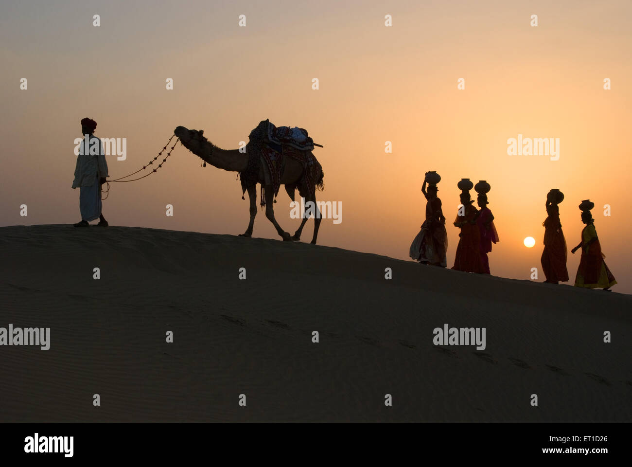 Men and woman with camel climbing up sand dune of khuhri ; Jaisalmer ; Rajasthan ; India Stock Photo