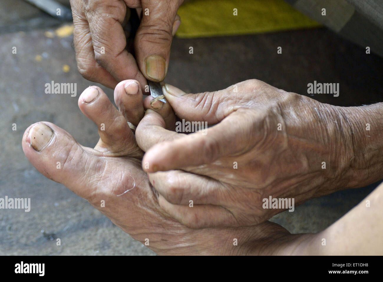 Man cutting the nail of finger of foot on footpath Kolkata West Bengal India Asia Stock Photo