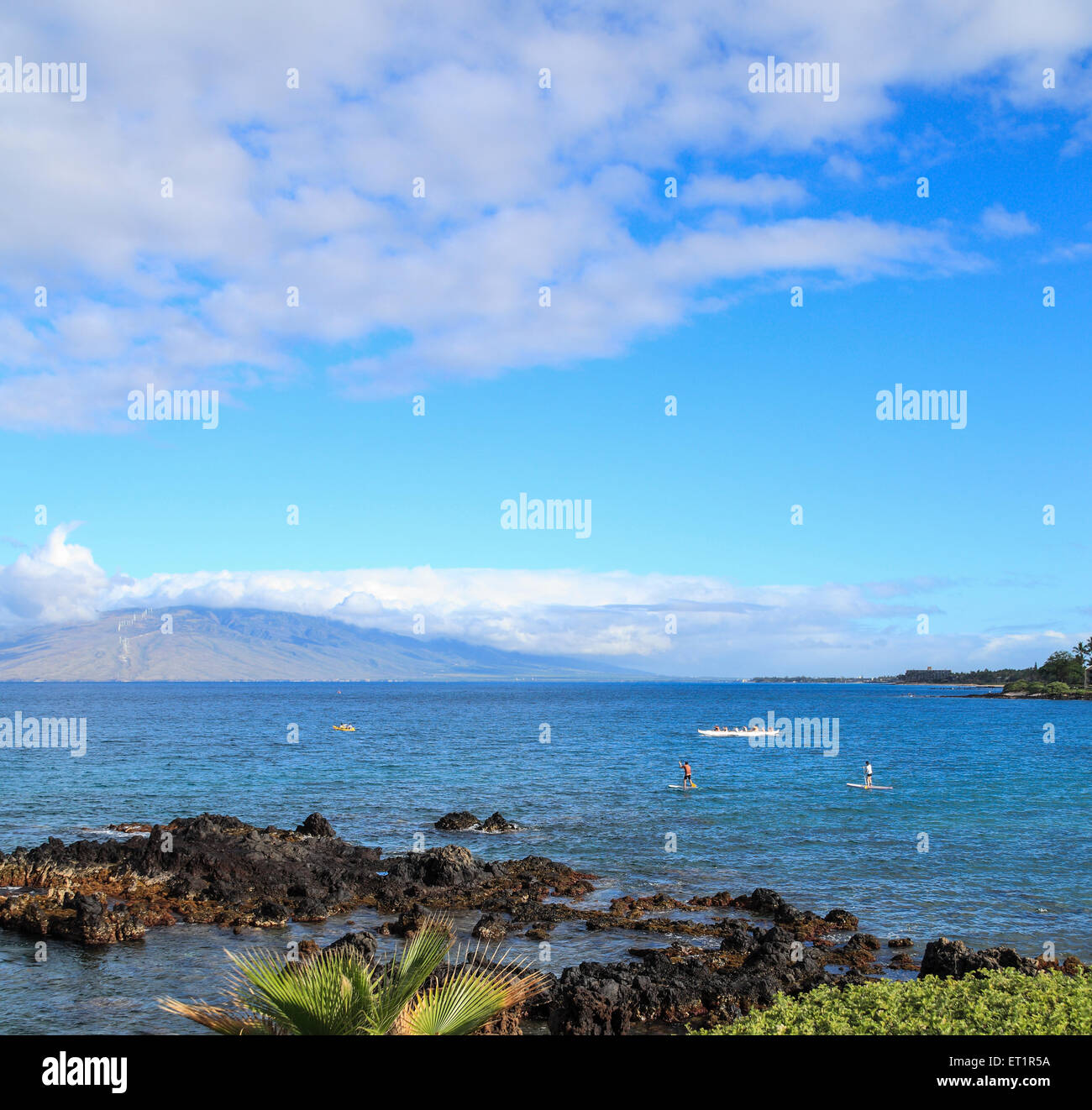 Stand up paddleboarders, kayakers and outrigger canoe tour off Wailea Beach, Maui, as viewed from the beach walk Stock Photo