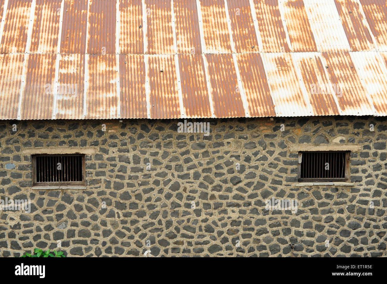 Stone wall with windows and rusted metal roof ; Akluj ; Solapur ; Maharashtra ; India Stock Photo