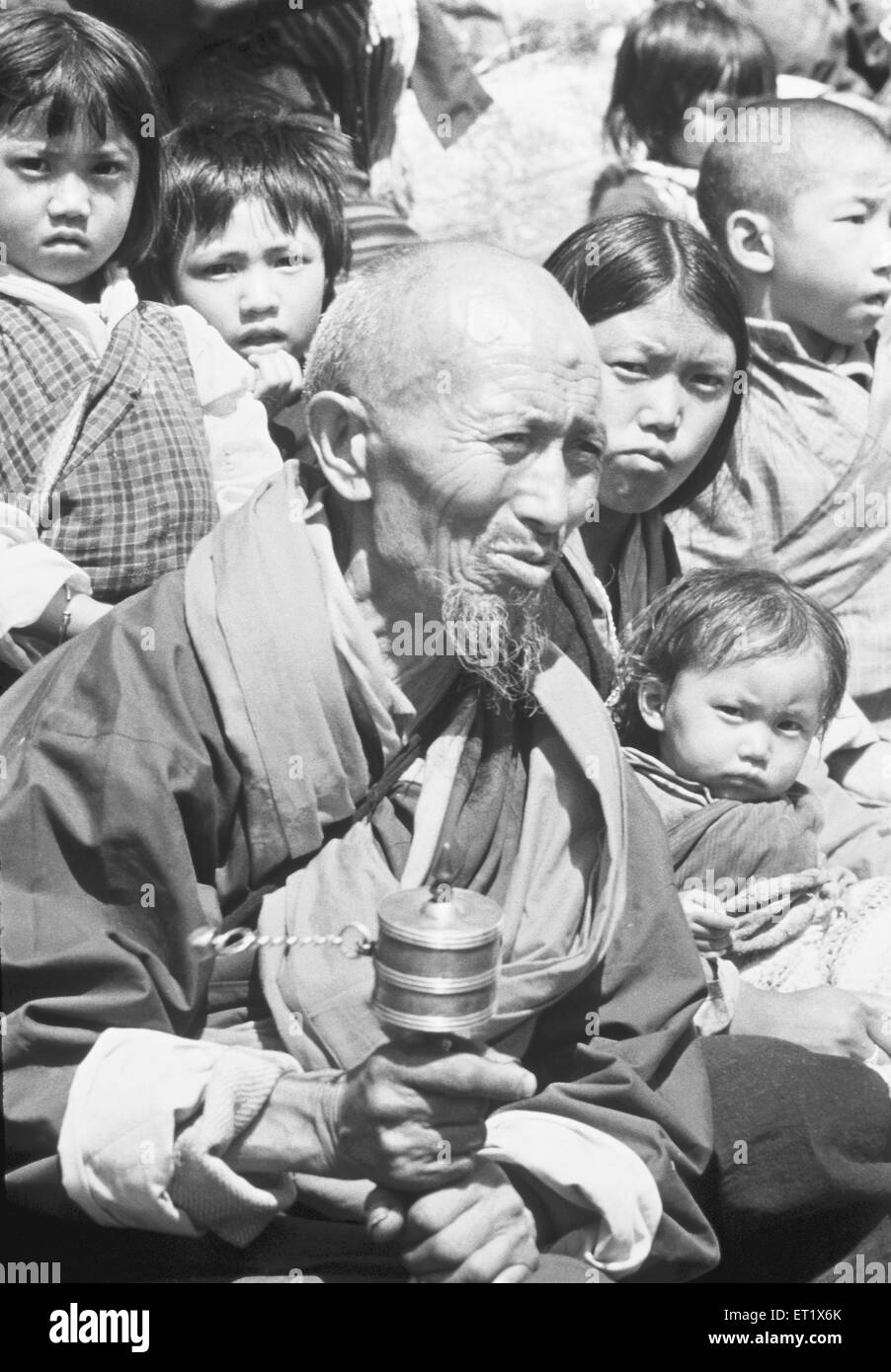 Old man dressed in traditional costume turns the prayer wheel at festival ; Bhutan Stock Photo