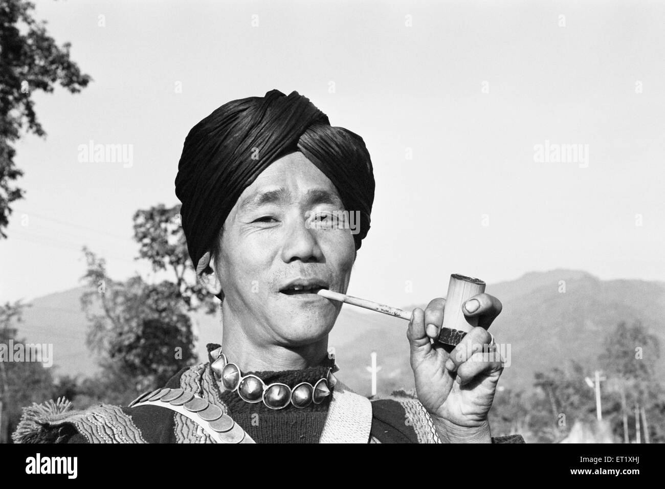 Tribal man belonging to Mishmi tribe smoking using pipe in Arunachal Pradesh ; India 1982 NO MR Stock Photo