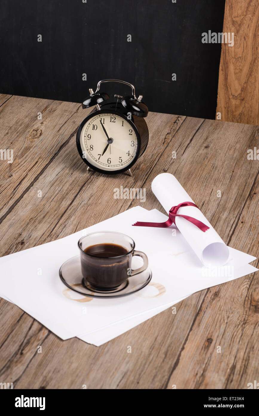 Old clock, hat, coffee and paper sheets on old Wooden table. Stock Photo