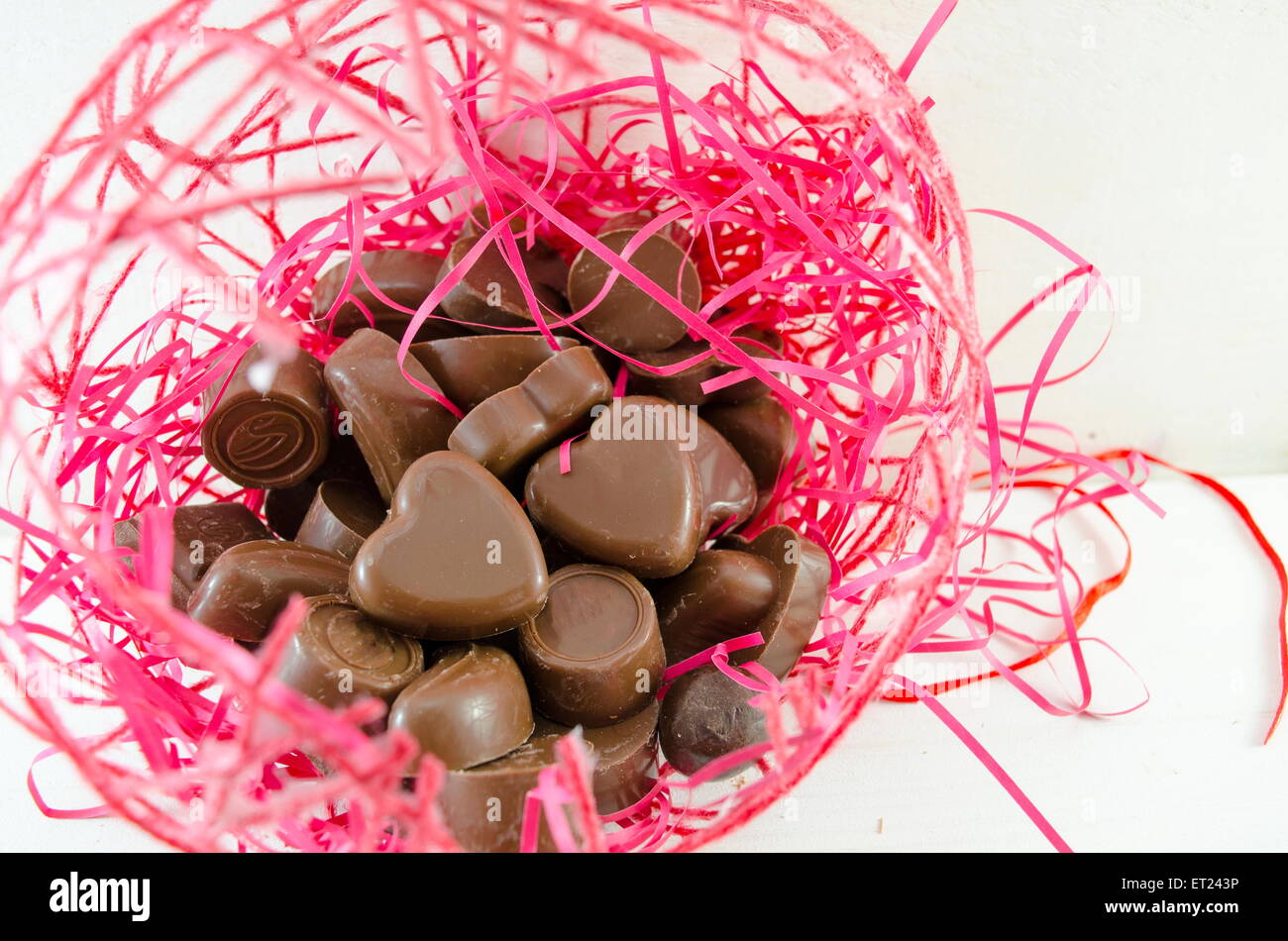 Chocolate hearts in a pink nest against a white surface Stock Photo