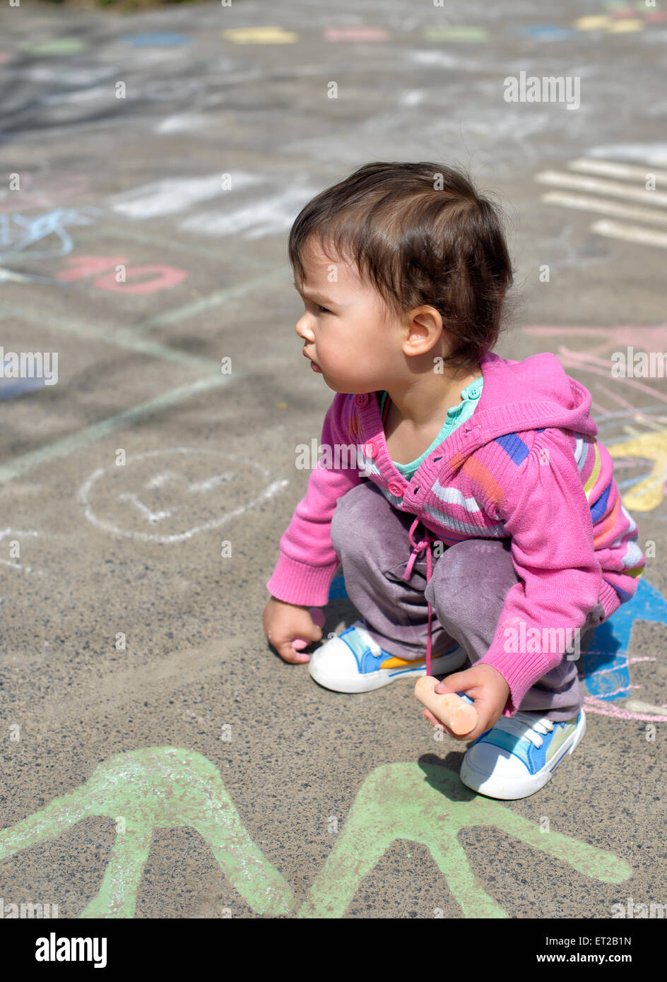 happy little girl draw with chalk on the pavement in the park Stock Photo