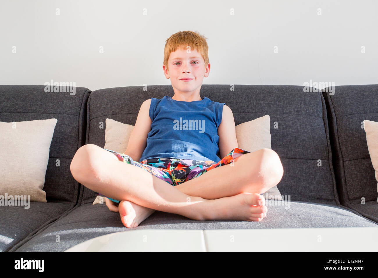 Young, confident red haired boy of seven lounging on the sofa indoors Stock Photo