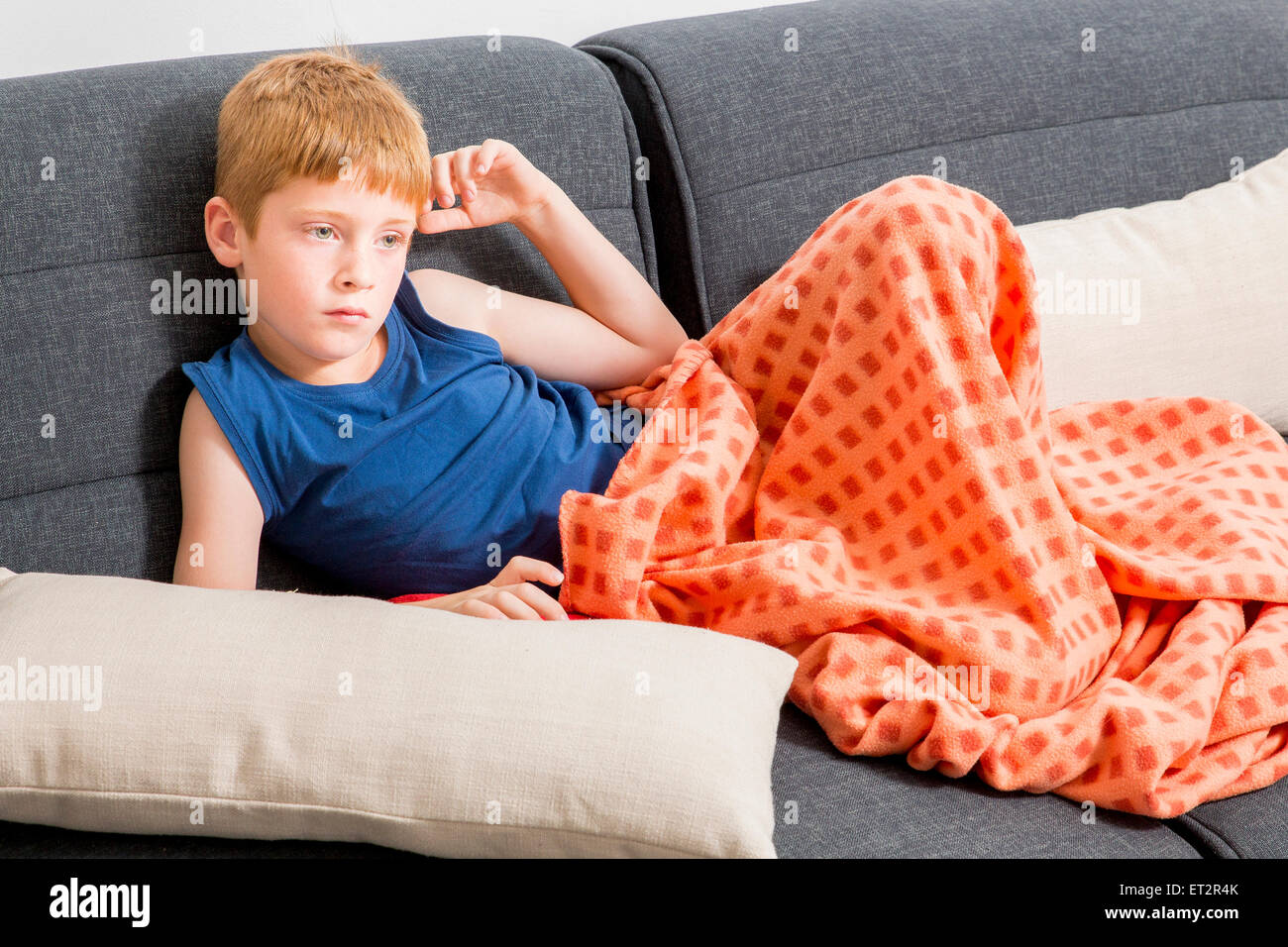 Young, sad, red haired boy of seven lounging on the sofa indoors Stock Photo